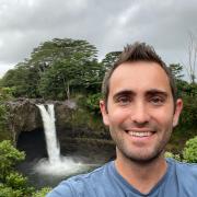 a selfie of James standing near a waterfall