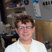 Connor wears a lab coat as he sits in a chair