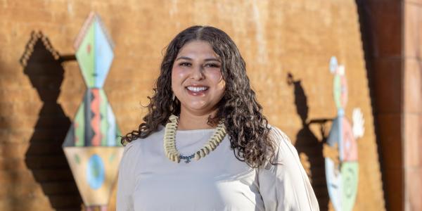 A woman with a large necklace in front of metal art on the side of a building