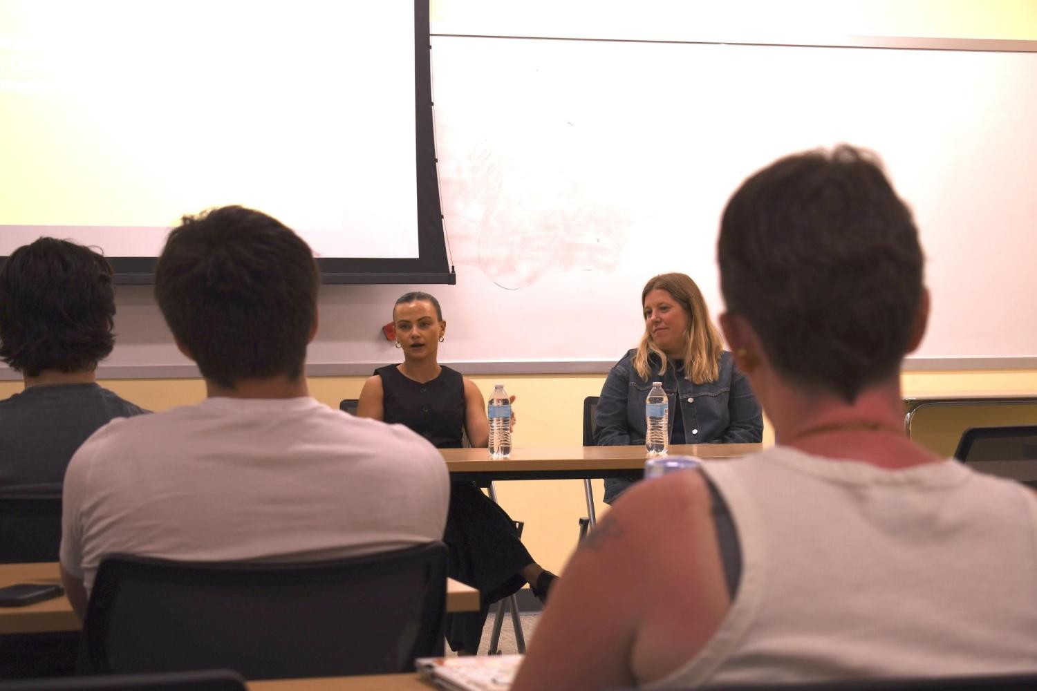 Shelby Cravens and Katie Stiffler sit at table talking to class
