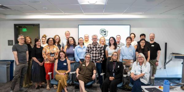 Group photo of the CU Denver Health Research Collaborative kickoff, with approximately two dozen participants gathered in a conference room, standing and seated in front of a screen displaying the CU Denver logo.