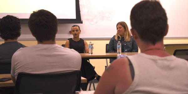 Shelby Cravens and Katie Stiffler sit at table talking to class