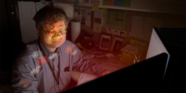 Hai Lin sits in front of glowing computer with imagery of atoms