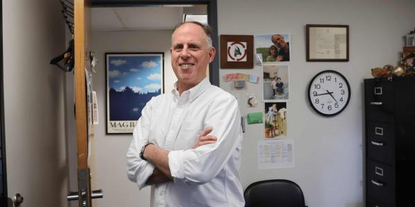 Professor David Hildebrand stands in his office in a white button up shirt.