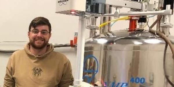 James Beham, CU Denver MS Chemistry Student, stands next to an NMR spectrometer.