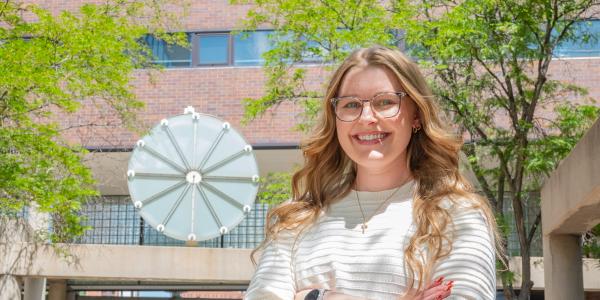 Kayley stands smiling with arms crossed in front of clock