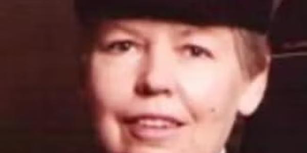 Professor Mary Rose Sullivan in a formal U.S. Navy uniform, wearing a white cap with gold trim and insignia, smiling slightly against a dark background.