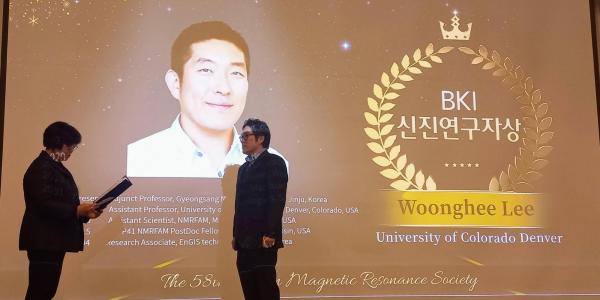 Professor Lee receiving the BKI Early Career Award, in front of a slide with his picture on it