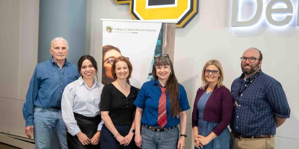 From left to right Jim Grigsby, Vanessa Navarro-Rodríguez, Anna Warrener, Nicky Beer, Lisa Keranen, and Michael Moore. They stand in front of a University of Colorado Denver sign and a banner for the College of Liberal Arts and Sciences 