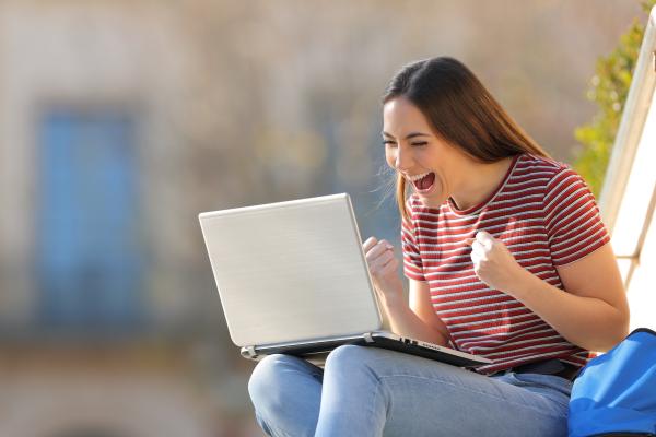 Enthusiastic online student smiling and fist pumping in front of her laptop