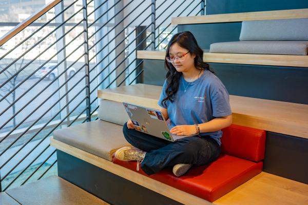 Abby sits in a stairwell working on a laptop