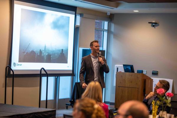 Ben Greenwood gives a presentation at CLAS Mixtape. He is wearing a grey blazer and a blue button up.