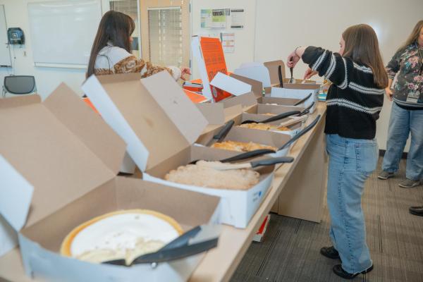 student stands at table cutting into pies