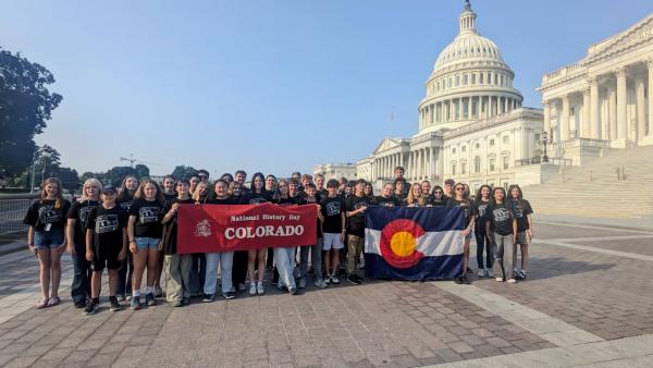 high school students stand in front of the US capitol building holding a National History Day Colorado flag