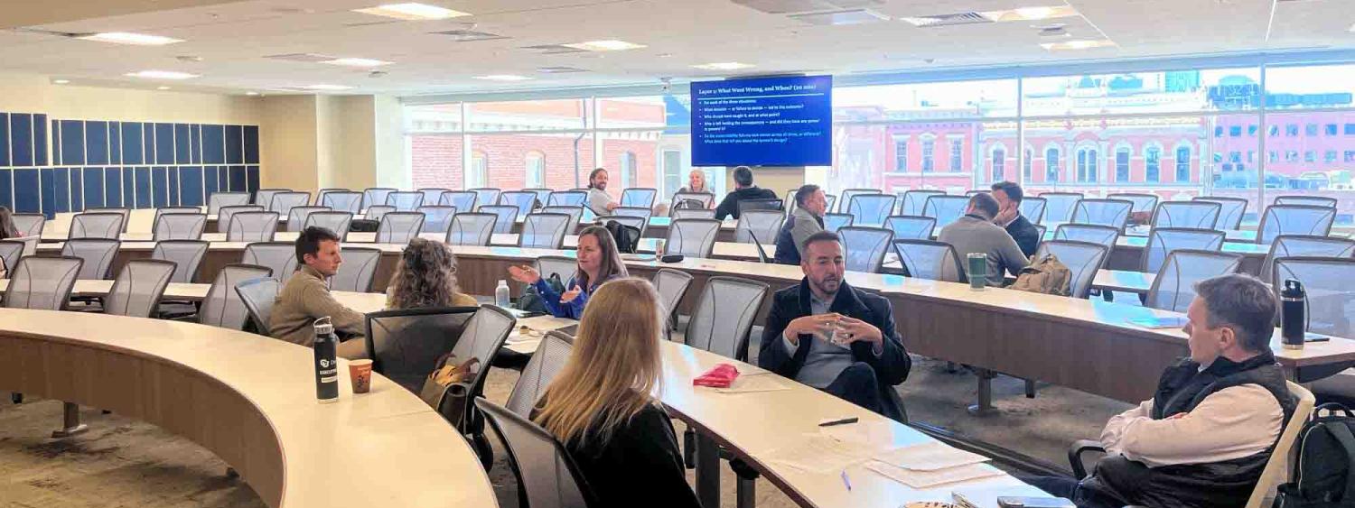  What Went Wrong, and When?" Large windows offer a view of downtown Denver buildings.