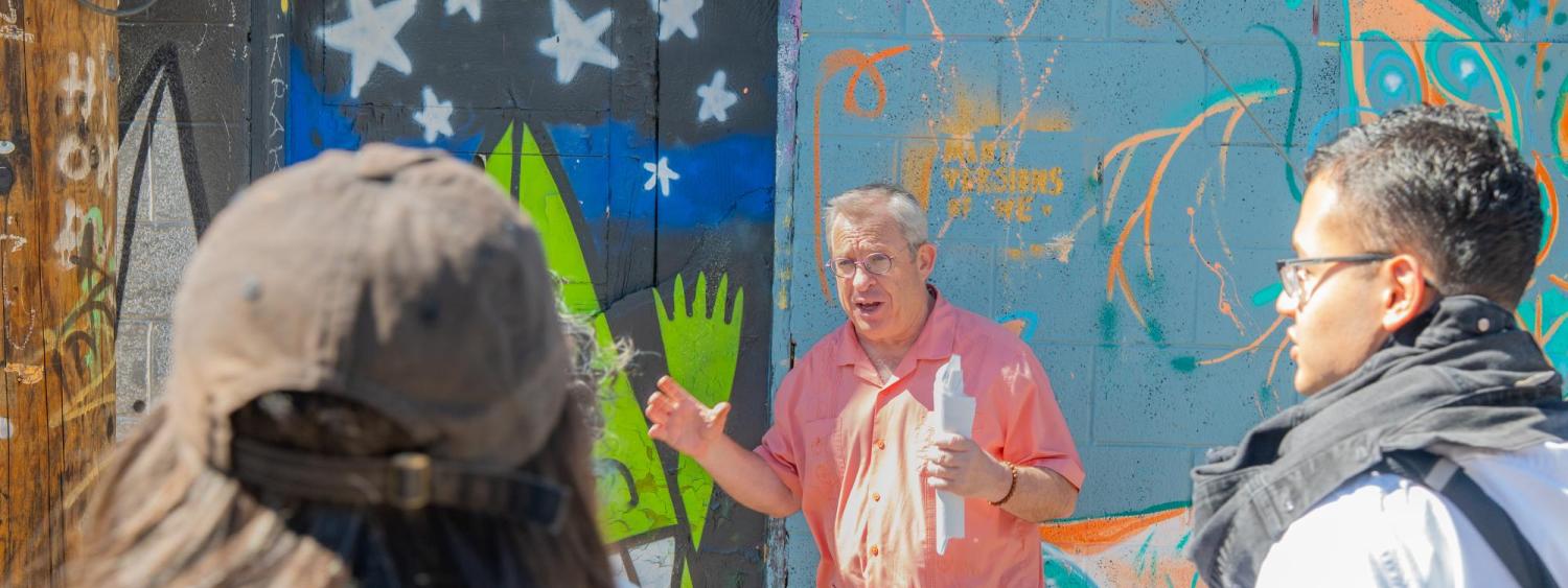 Prof. Tony Robinson speaks in front of mural