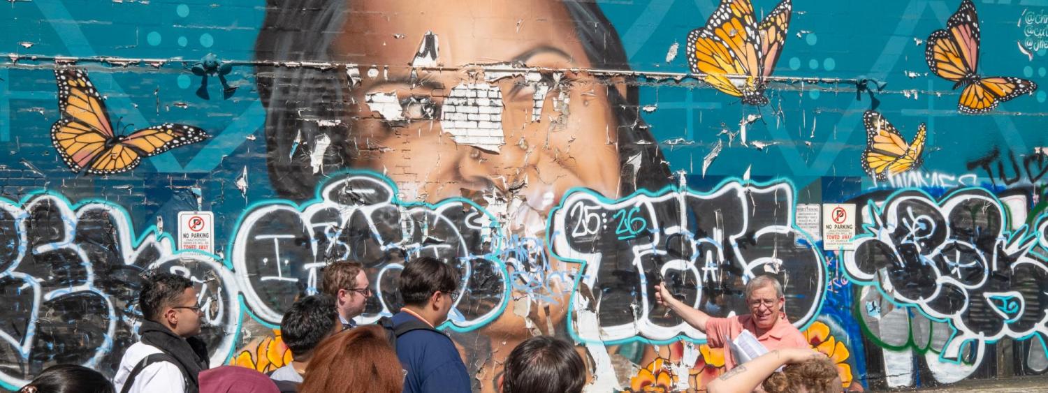 Prof. Tony talks in front of a torn up mural
