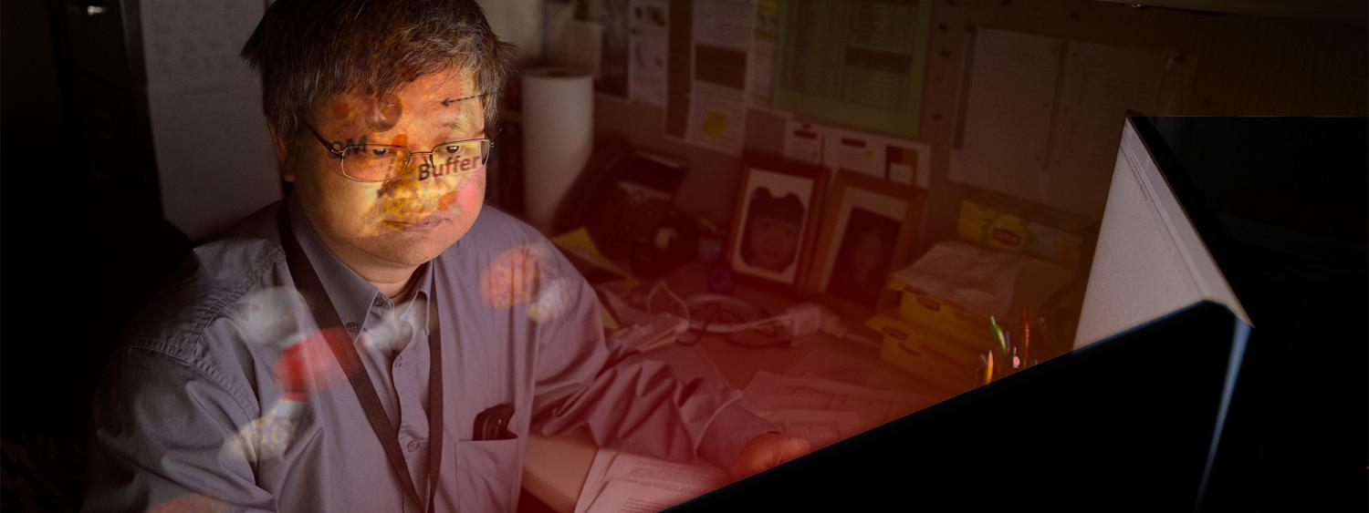 Hai Lin sits in front of glowing computer with imagery of atoms