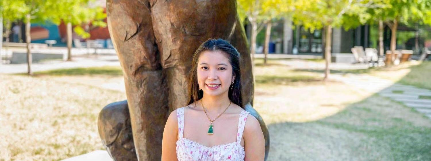 Kim Phun Van smiles in front of the CU Denver bronze lynx statue outside the Student Commons Building