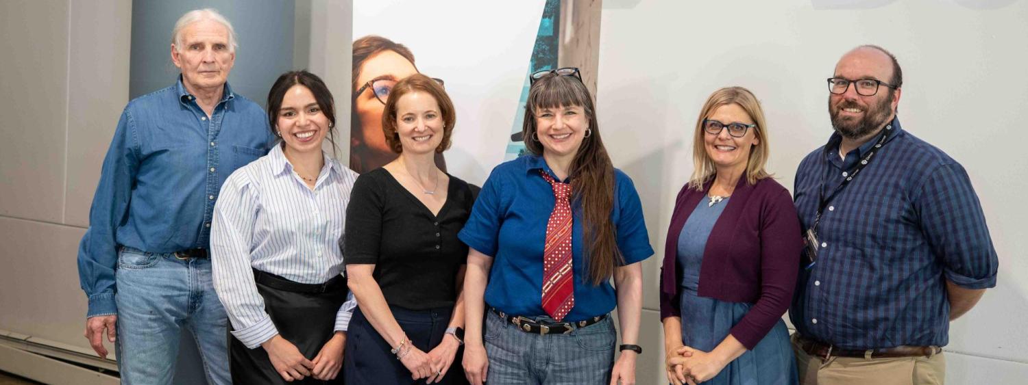 From left to right Jim Grigsby, Vanessa Navarro-Rodríguez, Anna Warrener, Nicky Beer, Lisa Keranen, and Michael Moore. They stand in front of a University of Colorado Denver sign and a banner for the College of Liberal Arts and Sciences 