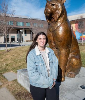 Alyssa Hohorst stands outdoors on the CU Denver campus beside the bronze Milo the Lynx statue.