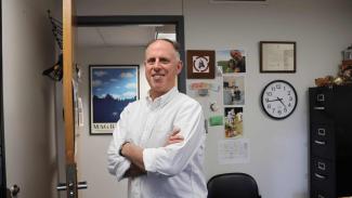 Professor David Hildebrand stands in his office in a white button up shirt.