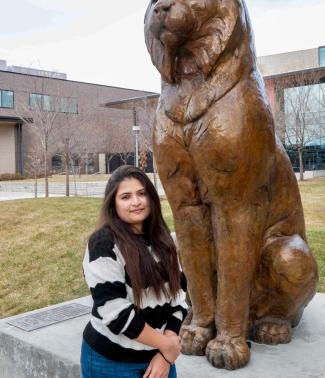 Indira Saha stands on the CU Denver campus next to Milo, the Lynx mascot statue, with campus buildings in the background