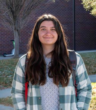 Jessica Loeffler stands outdoors on the CU Denver campus, smiling at the camera, with trees and a campus building in the background