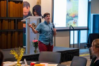 Rachel Gross gives a presentation at CLAS Mixtape. She is wearing red pants and a blue button up.