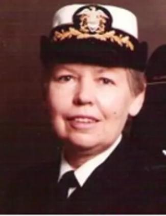 Professor Mary Rose Sullivan in a formal U.S. Navy uniform, wearing a white cap with gold trim and insignia, smiling slightly against a dark background.