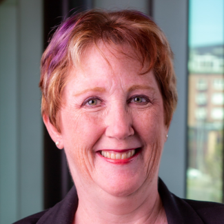 Kirsten smiles at camera, in an office building setting in a black shirt.