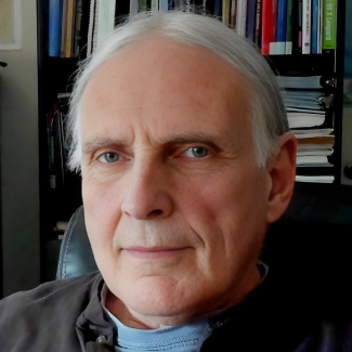 Jim Grigsby is pictured, with brown shirt, in front of a bookcase.