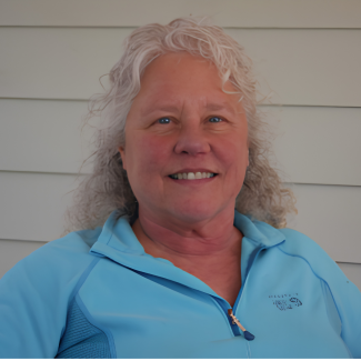 Doris smiles at camera, wearing a blue zip up shirt against a white backdrop.