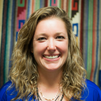 Amanda Ritchie smiles at camera, against a colorful backdrop in a blue shirt.