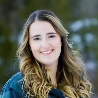 Kayla Spencer smiles in a forested area with a green shirt.
