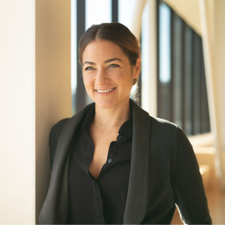 Esther Sullivan stands in a sunny hallway, wearing a black blazer.