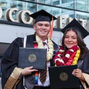 CU Denver graduates stand proudly with diploma covers in front of the Colorado Convention Center for the Fall 2025 Commencement Ceremony