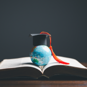 A globe with a graduation cap sits in a book to represent studying abroad