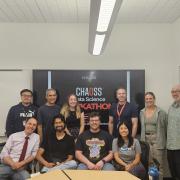 students and faculty of the hackathon sit a table smiling