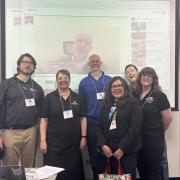 Carlock on the video screen behind CU Denver’s Kyle Danforth, Shana Medah, Sean Mueller, Regina Rodriguez, Stephen Hartnett, and Roxy New.