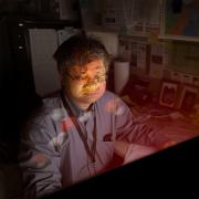 Hai Lin sits in front of glowing computer with imagery of atoms