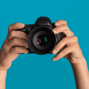 A camera held by a pair of hands iwth a blue background