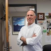 Professor David Hildebrand stands in his office in a white button up shirt.