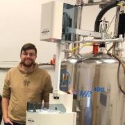 James Beham, CU Denver MS Chemistry Student, stands next to an NMR spectrometer.