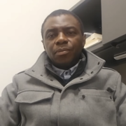 Olukayode Bakare sits in front of camera with Al Jazeera Logo in lower lefthand corner