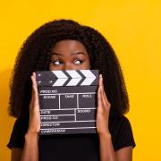 A student peeks from behind a film clapboard 