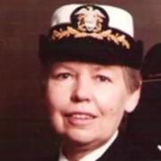 Professor Mary Rose Sullivan in a formal U.S. Navy uniform, wearing a white cap with gold trim and insignia, smiling slightly against a dark background.