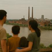 family stands along a river looking out towards a factory