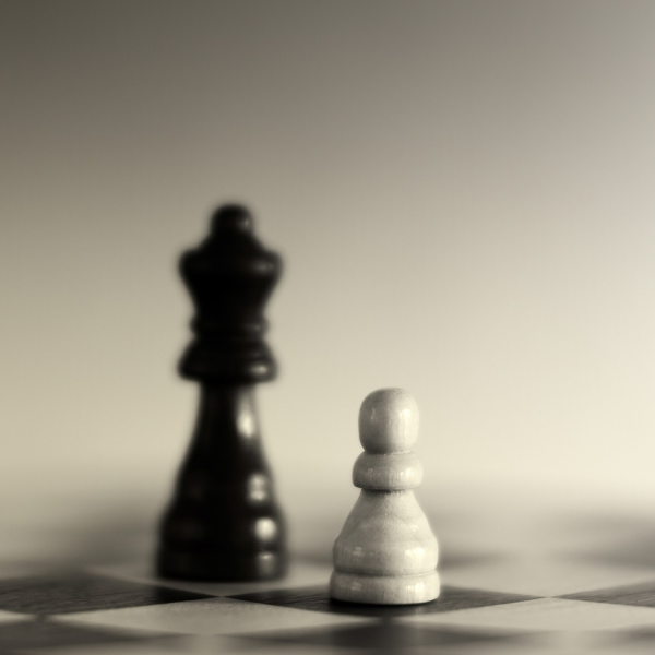 Black queen chess piece next to white pawn chess piece on chess board