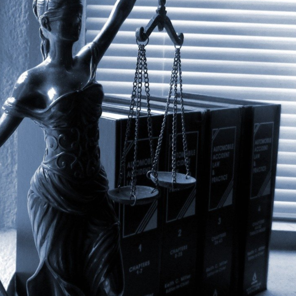 Grayscale desk with statue of blind justice, legal journals, and globe.